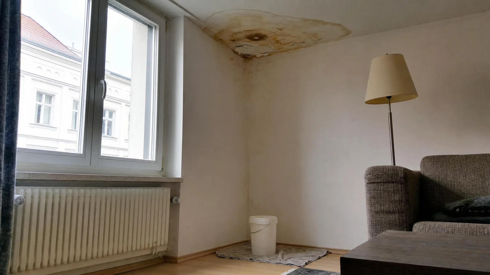 Wasserfleck an der Zimmerdecke, darunter ein Eimer auf einem Handtuch