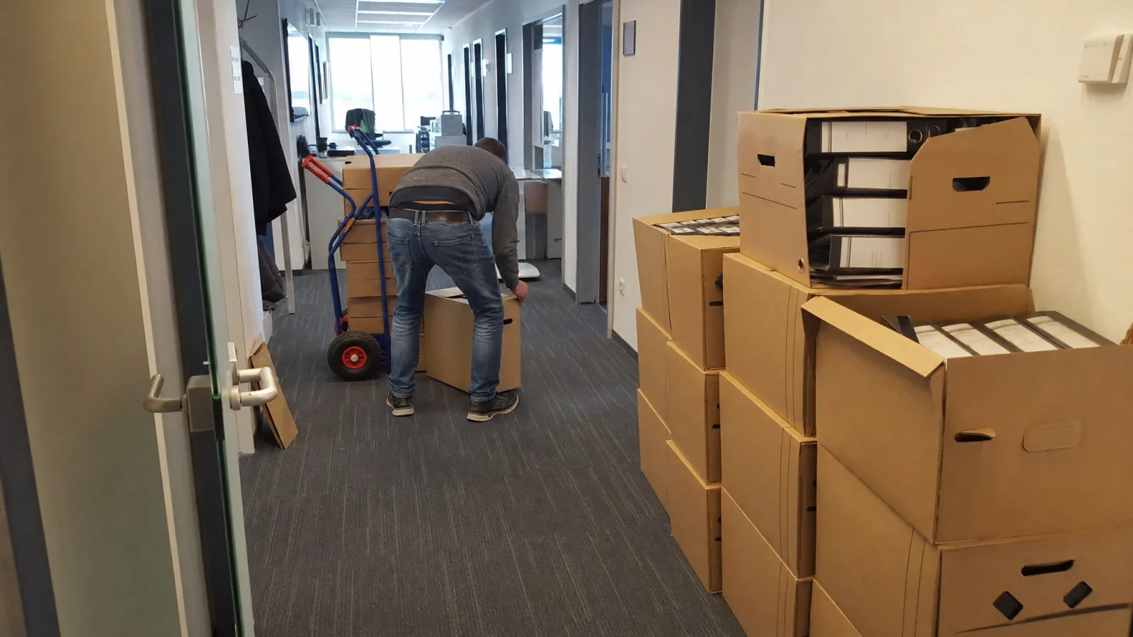 Archivkartons mit Aktenordnern werden im Büroflur umgezogen