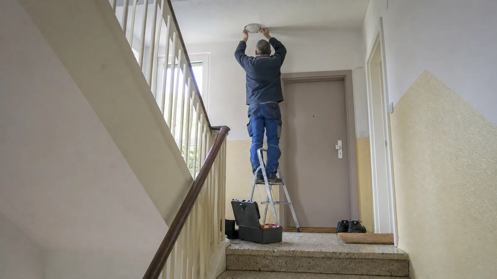 Hausmeister auf einer Leiter im Treppenhaus eines Altbaus