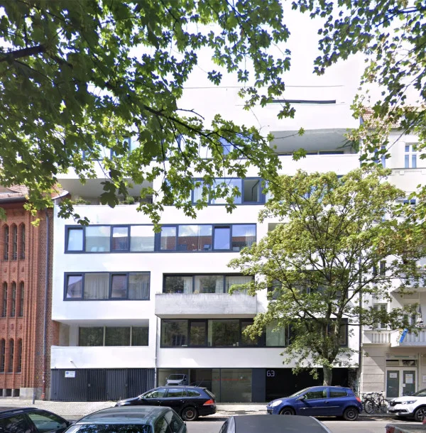 Modernes weißes Mehrfamilienhaus hinter Straßenbäumen an einer Berliner Straße